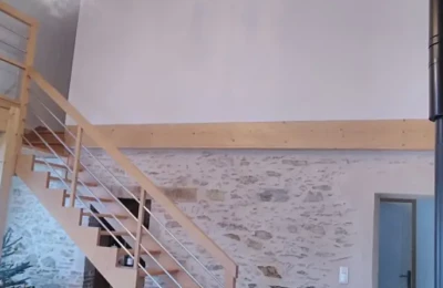 Un escalier en hêtre verni montant à la mezzanine dans cette pièce haute de plafond Un escalier montant sur une mezzanine contre un mur haut